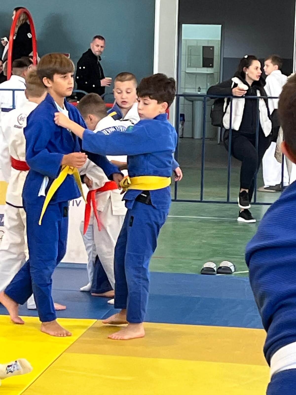 Doi copii în kimono albastru cu centură galbenă, prinși în priză pe tatami